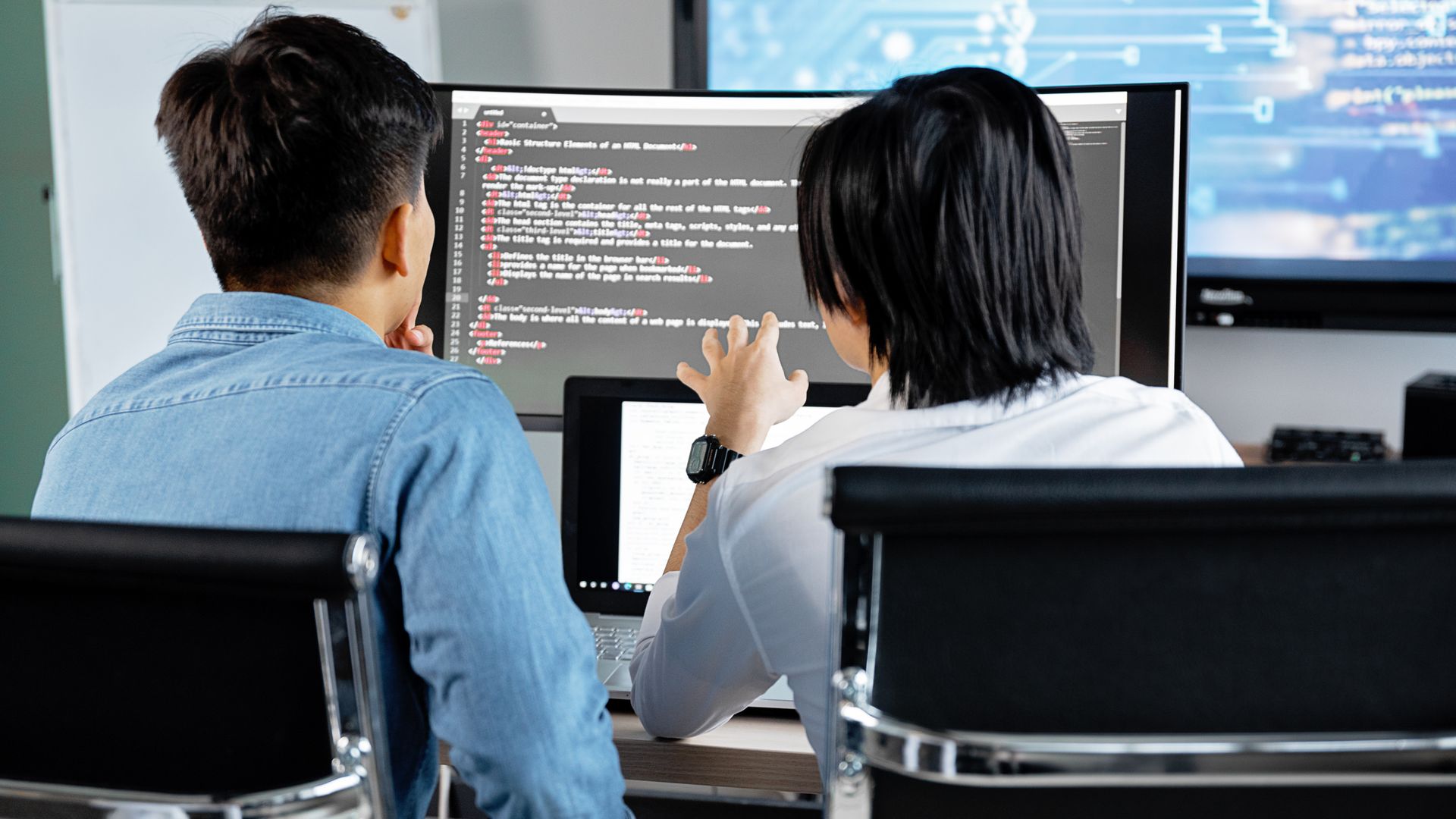 コードが表示されたモニターの前で打ち合わせする開発者